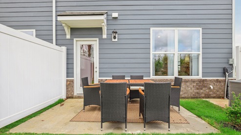 Outside of two story townhome with back patio decorated with table set and chairs for an outdoor meal