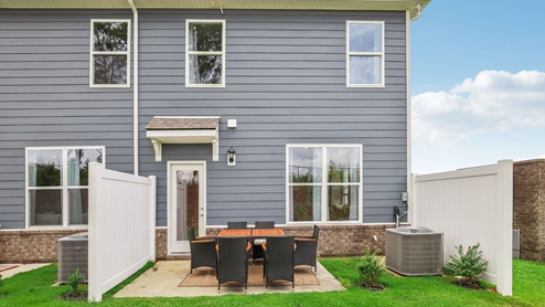 Outside of two story townhome with back patio decorated with table set and chairs for an outdoor meal