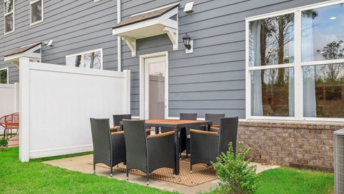 Outside of two story townhome with back patio decorated with table set and chairs for an outdoor meal
