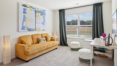 Carpeted loft area with a couch, side table, poufs for additional seating, and a craft table beneath the wall-mounted TV.