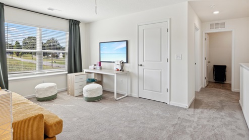Carpeted loft area with a couch, side table, poufs for additional seating, and a craft table beneath the wall-mounted TV.Carpeted loft area with a couch, side table, poufs for additional seating, and a craft table beneath the wall-mounted TV.