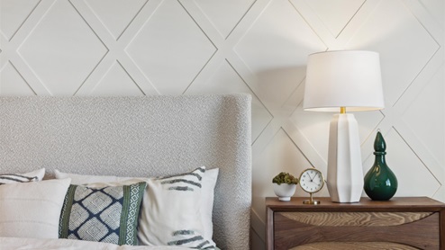 Primary bedroom with an accent wall with tonal lattice design, a bed with upholstered headboard, and a nightstand topped with a lamp and decor.