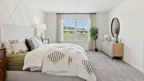 Primary bedroom with carpeted floors, a large bed flanked by nightstands, a dresser on the opposite wall, and a double window allowing lots of natural light to flood in.