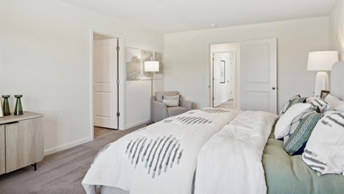 Primary bedroom with a large bed, storage console, and an armchair with floorlamp.