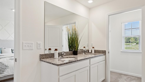 Primary bathroom with a double vanity with dark countertops upon white, shaker-style cabinetry.