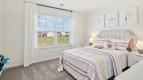 Secondary bedroom decorated in pastel colors with a double bed flanked by nightstands beneath cheerleader artwork on the wall.