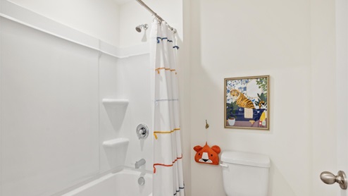 Secondary bathroom with tiger in a bathtub artwork and a striped shower curtain enclosing the tub-shower combo.