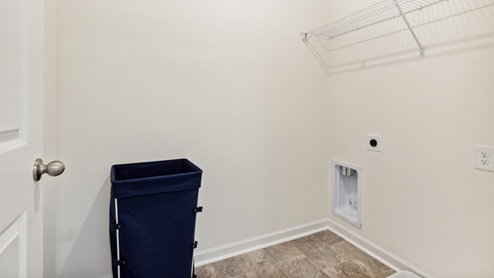 Laundry room with tiled floor, hookups for a full-sized washer and dryer, and a shelf above for added storage.