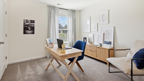 Secondary bedroom outfitted as an office with a desk and desk chair, accent chair in the corner, storage console, and various artwork and decor.