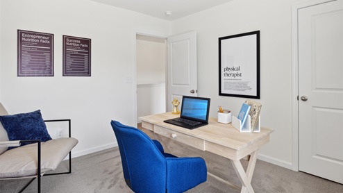 Secondary bedroom outfitted as an office with a desk and desk chair, accent chair in the corner, storage console, and various artwork and decor.