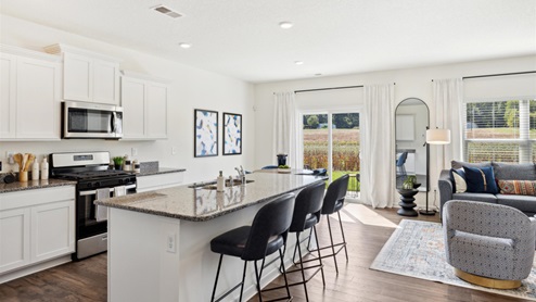 Kitchen with white, shaker-style cabinetry, granite countertops, and stainless-steel appliances, with a view of the dining area and sliding-glass doors leading onto the back patio in the background.