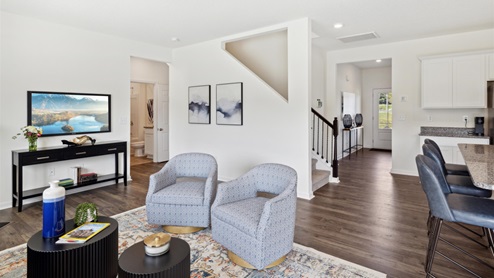 A living room with two club chairs facing the coffee table and a view down the entryway and across to the secondary bathroom in the background.