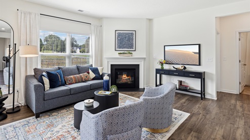 Living room with two club chairs across from a couch with a coffee table between, a console table beneath a wall-mounted TV, and a corner fireplace with white mantel and slate surround.
