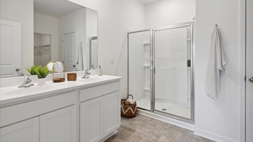 primary bathroom with white vanity, double sinks, and clear shower door