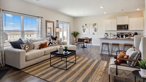 Living room with large window behind white couch and small black coffee table on the left, dining room and kitchen on the right