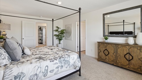 Master bedroom with black framed king size bed on the left ,open hallway door to the left, open bathroom door on the right next to console table
