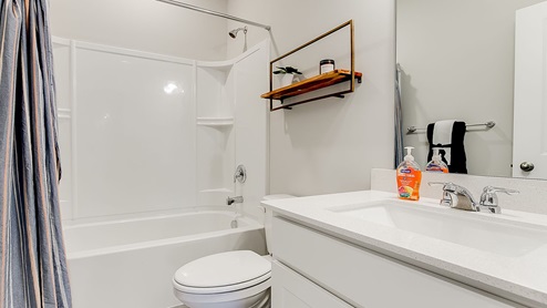 Main level bathroom with white cabinets and quartz vanity countertop.