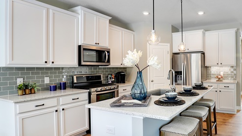 Kitchen with white cabinets, gray backsplash, and pendant lighting.
