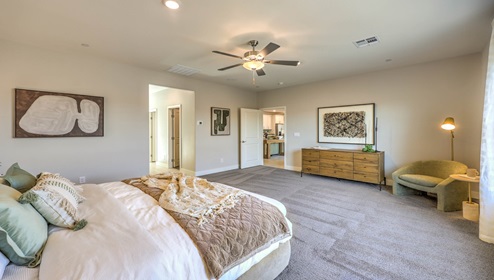The Bedroom One Suite in our Symmetry Manor 2538 model with carpet flooring, large windows, a walk-in closet, and a ceiling fan with a light kit.