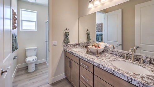 Bathroom Two in our Heartland Summit 4425 model with granite countertops at the double Bath Vanity, a walk-in shower, mirror, and brown cabinets.