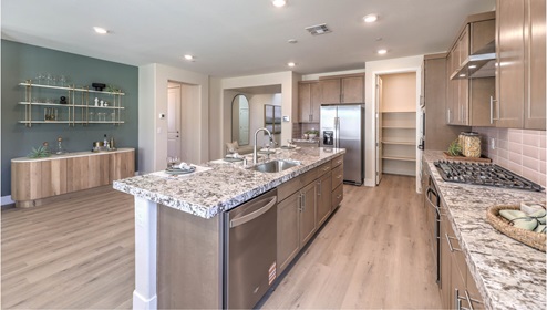 Our 4425 model kitchen in the Heartland Summit Community with brown shaker style cabinets, quartz countertops, a kitchen island, 5-burner cooktop, large pantry, and Whirlpool Stainless Steel appliances.