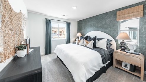 Primary bedroom in one of Phoenix's model homes with a large bed flanked by two nightstands and backed by an accent wall and a dresser across from the foot of the bed.