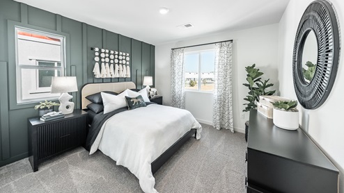 Primary bedroom with a large bed, two nightstands, a dresser, and a stunning accent wall with carpentry accents in one of Phoenix's model homes.
