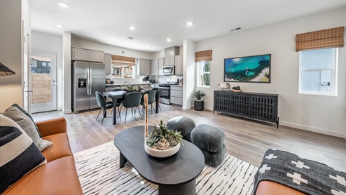A view from Phoenix's model home's living area towards the kitchen, which boasts gray, shaker-style cabinetry, stainless-steel appliances, and a dining table surrounded by 6 chairs.