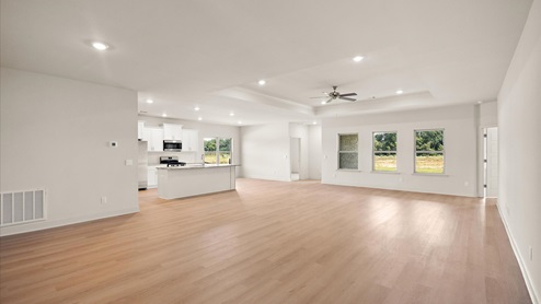 A spacious open floor plan living room, large windows, hardwood floors, and tray ceilings.