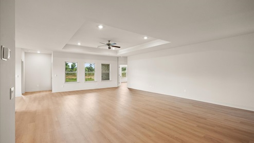 A spacious open floor plan living room, large windows, hardwood floors, and tray ceilings.
