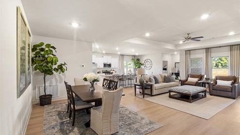 A spacious open floor plan living room, large windows, hardwood floors, and tray ceilings.