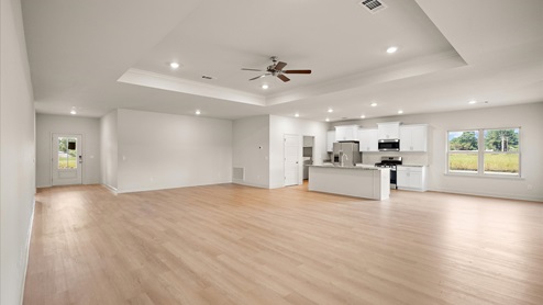 A spacious open floor plan living room, large windows, hardwood floors, and tray ceilings.