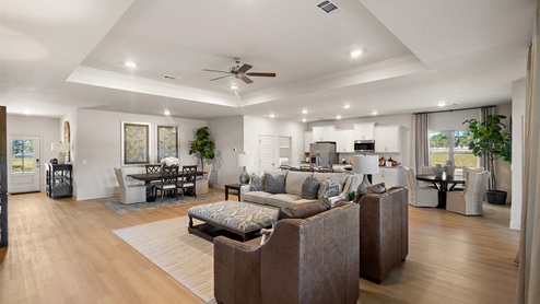 A spacious open floor plan living room, large windows, hardwood floors, and tray ceilings.