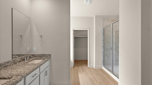 A modern bathroom featuring a double vanity with granite countertops bright light fixtures, and walk in shower