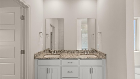 A modern bathroom featuring a double vanity with granite countertops, and bright light fixtures