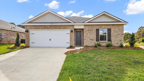 Freeport floorplan in the Foxwood community in Jackson, MS. Front exterior single story home with red/brown brick and white paneling and black shutters on the windows with side walk to the front door. The two-car garage and driveway.