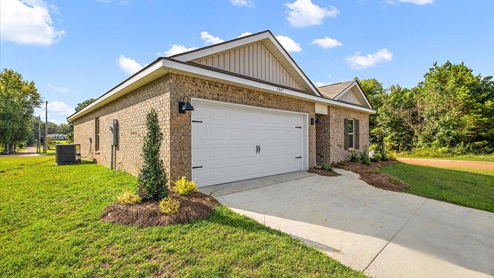 Side exterior single story home with multi color brown brick and white paneling and brown shutters on the windows with side walk to the front door. The two-car garage and driveway.