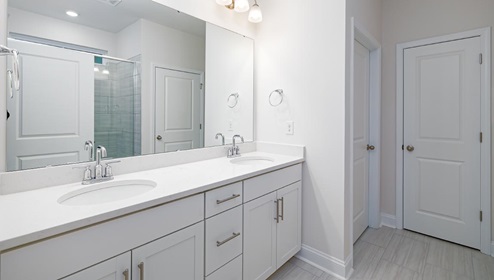 Primary bathroom with double sink vanity, white counters and cabinets, and standing glass door shower