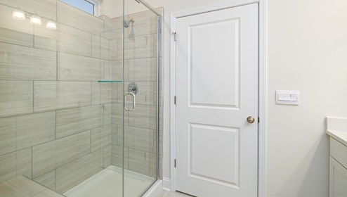 Primary bathroom with double sink vanity, white counters and cabinets, and standing glass door shower