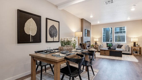 Scholls Meadow dining room with a dining room table with four chairs, a rug, two paintings, and an open concept great room with a white couch, electric fireplace, and end tables