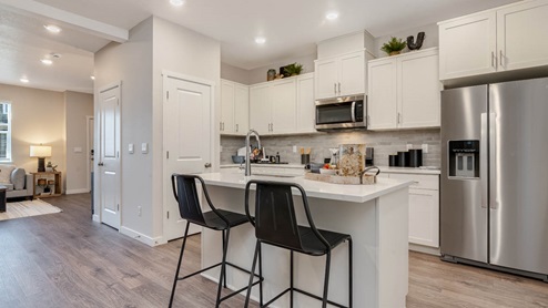Scholls Meadow kitchen with an island, stainless steel appliances, white shaker cabinets, quartz countertops, an open concept living room with a staircase