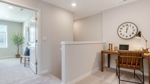 Scholls Meadow tech niche with brown desk with laptop and books, desk chair, carpet, and hallway to primary bedroom