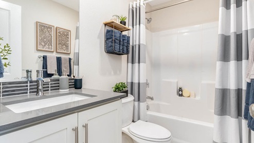Scholls Meadow secondary bathroom with quartz countertops, mirror, white shaker cabinetry, white shower tub, and hanging decorations