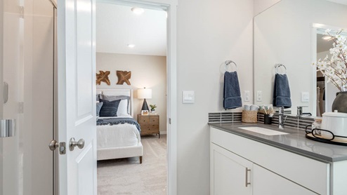 Scholls Meadow primary bathroom with quartz countertops, double vanity, mirror, window, and walkway into primary bedroom