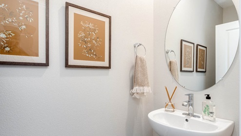 Scholls Meadow Powder room with single sink vanity, oval mirror, soap, white walls, fragrance scent, towel, paintings
