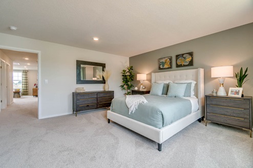 Marcola Meadows Primary bedroom with green accent wall, corner chair, green and white bedding, brown wooden furniture, and light beige carpeting