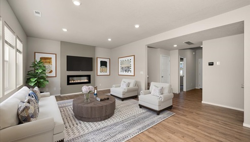 A living area with a light patterned rug, a white couch with matching accent chairs, a wooden ottoman, and three large windows letting in natural light.