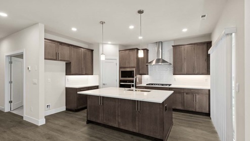 Kitchen of open concept main floor, featuring dark wood-style cabinets, quartz countertops, stainless steel appliances and tile backsplash