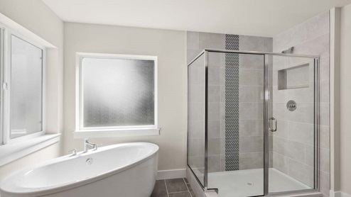 Modern freestanding soaking tub next to glass front step-in shower with full height ceramic tile and vertical accent strip