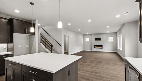 Alternate view of Baker floor plan kitchen quartz countertop island looking out to dining and living spaces, refrigerator nook and nearby stairwell